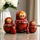 Round hand-painted Russian nesting dolls with red floral pattern displayed on a glossy table beside a white flower vase, traditional wooden Matryoshka set of 5.