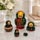 Traditional Khokhloma Russian matryoshka nesting dolls set of 5 displayed opened and closed on a polished marble table in a modern home interior. Hand-painted wooden nesting dolls with wild strawberries, green leaves, gold floral accents, glossy finish, and traditional folk art design.