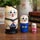 Hand-painted Russian cat sailor matryoshka dolls displayed as a set of three wooden nesting dolls, with the largest cat in a black sailor outfit and smaller cats dressed in blue and pink, photographed with a yellow vase and decorative napkin holder