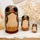 Three owl-shaped Russian nesting dolls arranged on a decorative table beside delicate dried flowers, showing their gray, cream and warm ochre painted details