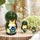 A charming set of three green frog nesting dolls displayed on a wooden slice, with hand-painted floral details and a soft botanical background