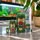 Five hand-painted green frog nesting dolls displayed on a marble tabletop, with a softly blurred aquarium and houseplant in the background