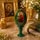 Green wooden Orthodox Easter egg with the Nursing Mother of God icon reproduction on a matching stand, displayed in a church-inspired setting with embossed metallic gold details and a glossy lacquer finish.